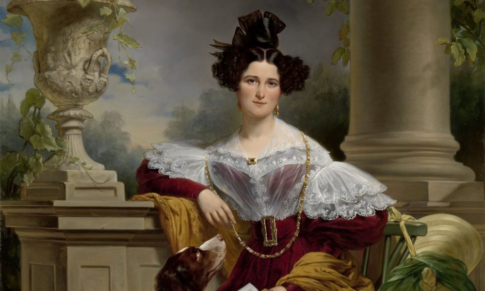 A woman in a red dress with a white lace collar. She is sitting in a garden setting.