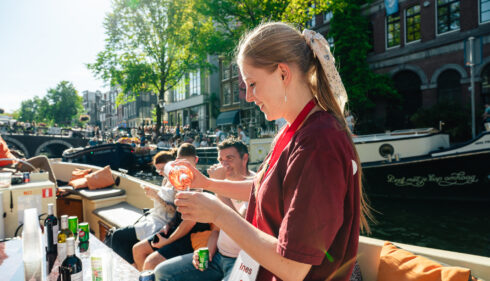 Woman on a boat. A canal with buildings and trees in the background.