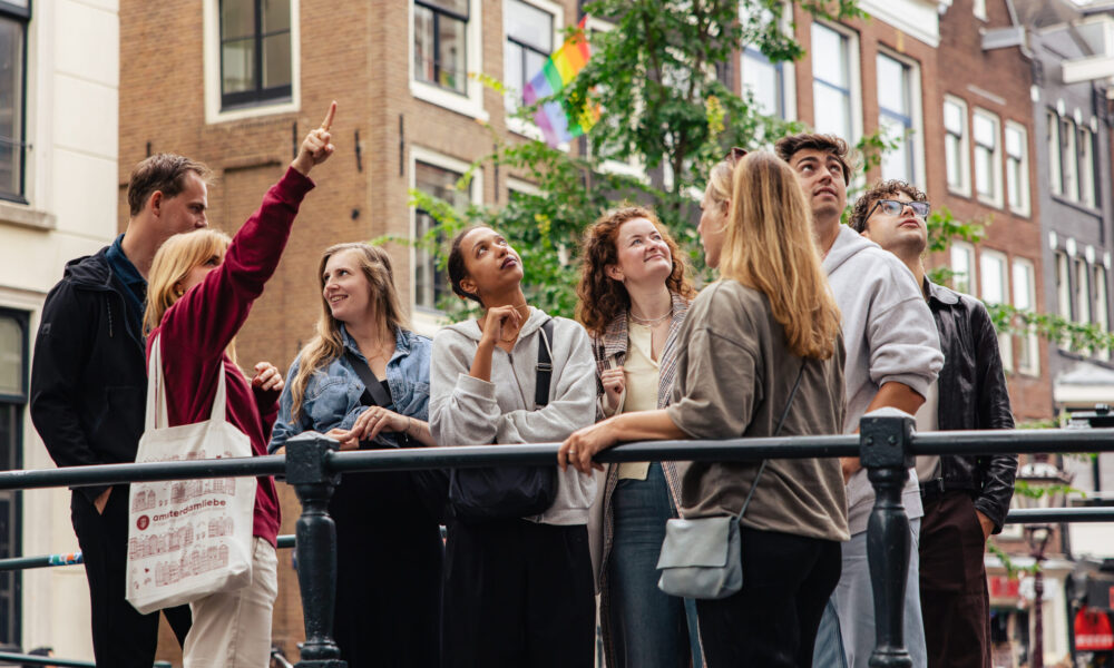 Group of young tourists on a city trip in Amsterdam. They are standing on a bridge looking around.