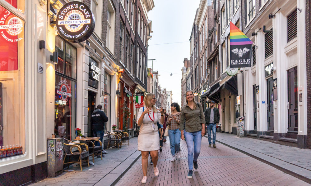 People walking down a street in Amsterdam. Colourful buildings and a rainbow flag.