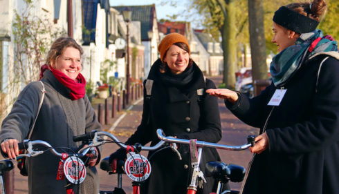 Tourist and guide talking while standing with bikes on Amsterdam street. Smiling women enjoying a bike tour.
