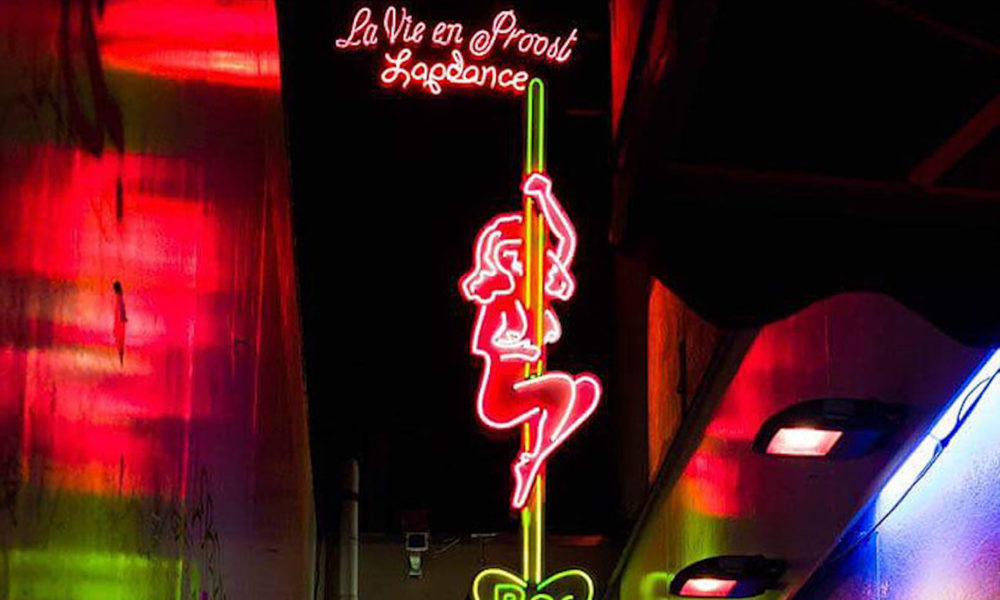 A neon sign featuring a pole dancer. The sign reads La Vie en Prostituée