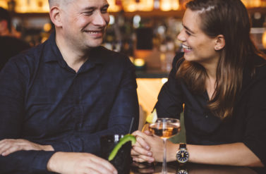 A man and woman enjoying a romantic evening together. They are sitting at a bar with drinks.