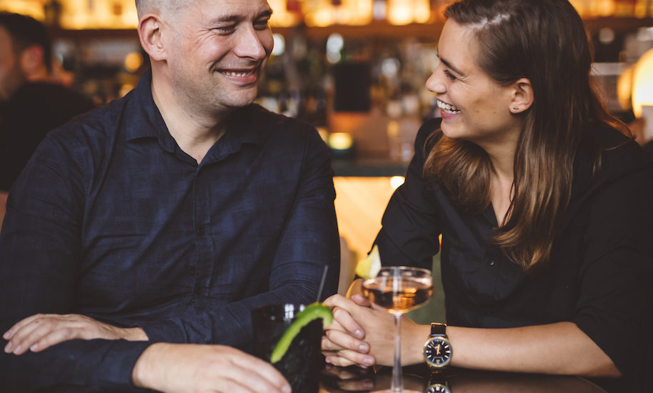 A man and woman enjoying a romantic evening together. They are sitting at a bar with drinks.