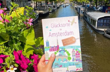 A travel guide to Amsterdam with a canal view. Boats and flowers in Amsterdam.