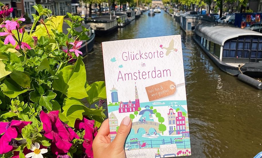 A travel guide to Amsterdam with a canal view. Boats and flowers in Amsterdam.