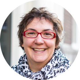 Portrait of a smiling woman with red glasses. She has short hair and a warm expression.