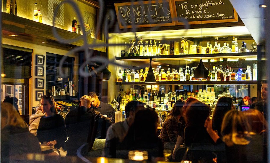 Le persone siedono nell'atmosfera accogliente e buia del Vesper Bar Amsterdam per gustare i cocktail.