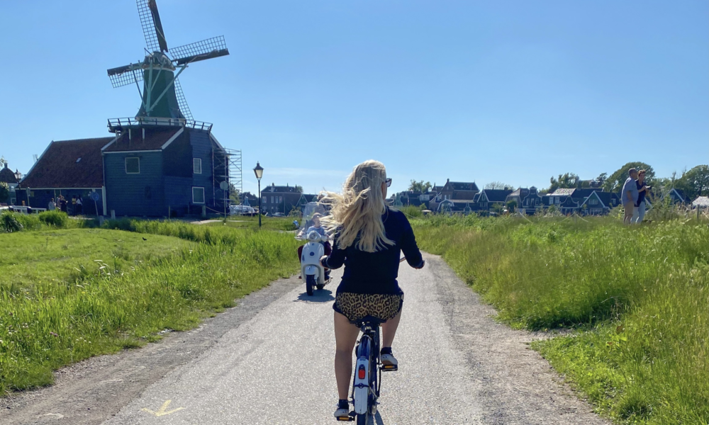 Woman cycling on a path with a windmill in the background. A picturesque scene in the Dutch countryside.