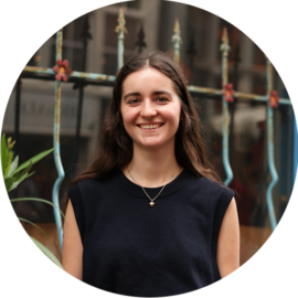 A young woman smiling at the camera. She is wearing a black top and a necklace.