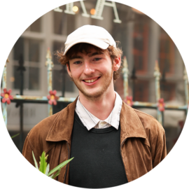 A smiling young man wearing a white cap and brown jacket