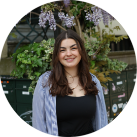 Portrait of a young woman smiling. She is standing outside.