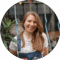 A smiling woman with long hair wearing dungarees. She is outdoors.