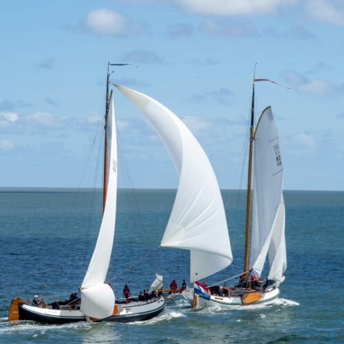Two white sailing boats racing on water. People on board enjoying the ride.