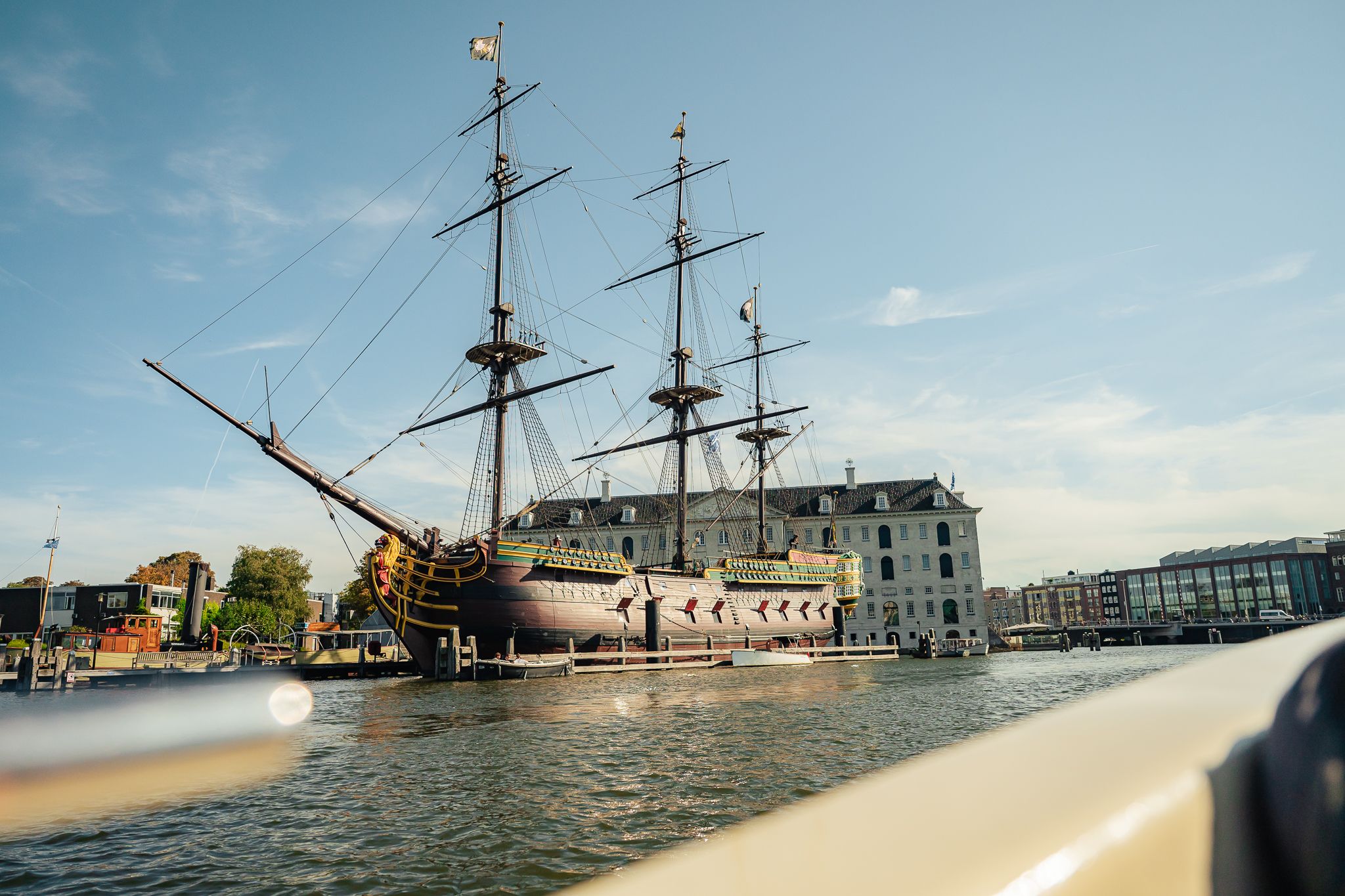 A historic ship docked in Amsterdam harbour. The vessel has multiple masts and a classic design.
