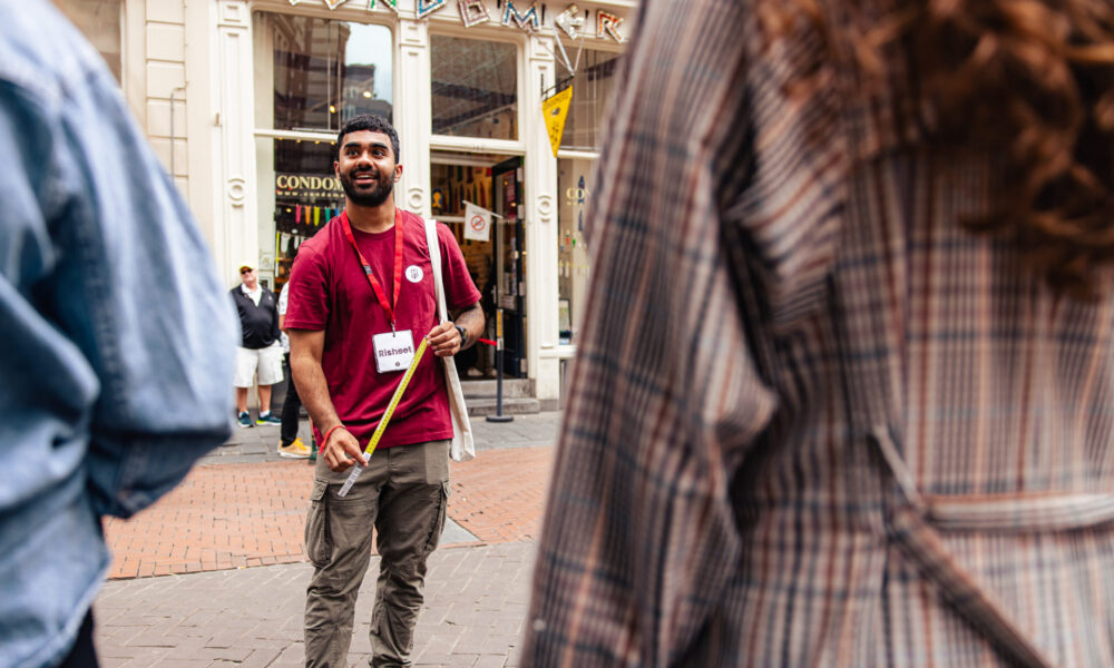 Tour Guide Risheet in a red shirt and a name tag with the name Risheet on it guides a tour through the Red Light district.